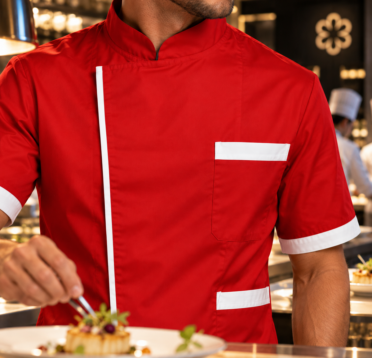 Chef con giacca 78525 rossa con bordi bianchi mentre completa un piatto in cucina.